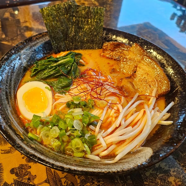 A bowl of Delish Kitchen 108 ramen with pork, egg, noodles, sprouts, green onions, and seaweed.