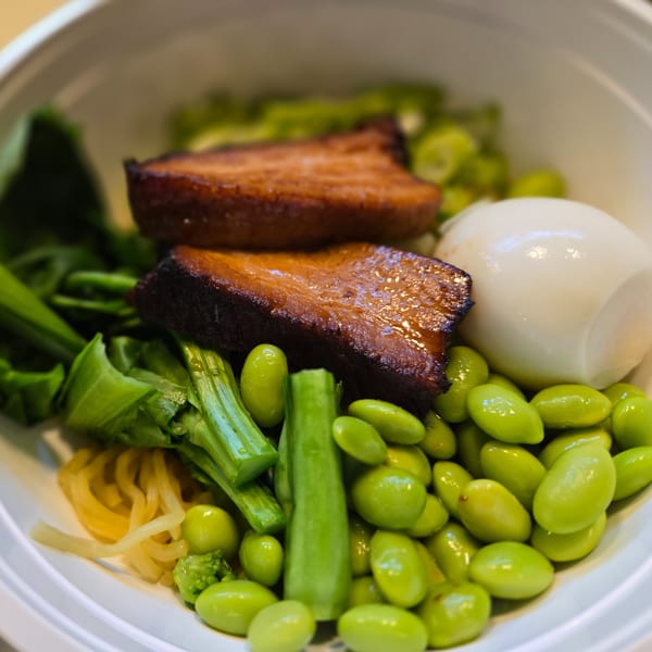 Close-up of a bowl with seared meat, edamame, green vegetables, and a hard-boiled egg.