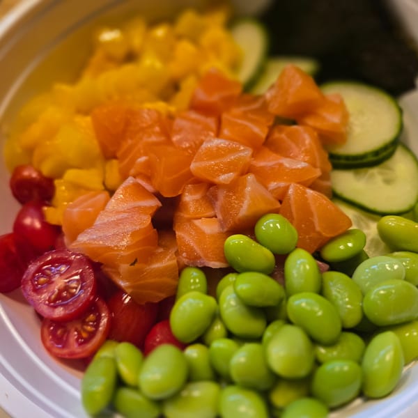 Colorful poke bowl with salmon, mango, edamame, cherry tomatoes, and cucumber slices.